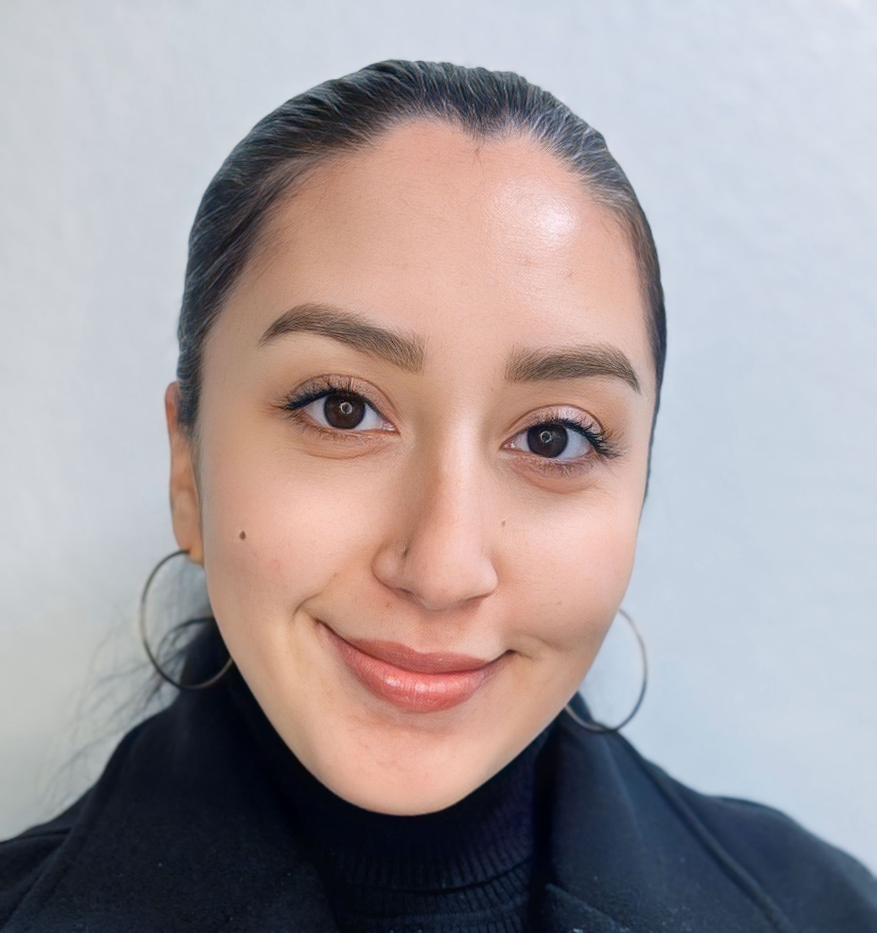 Person with hoop earrings smiling against a plain background.